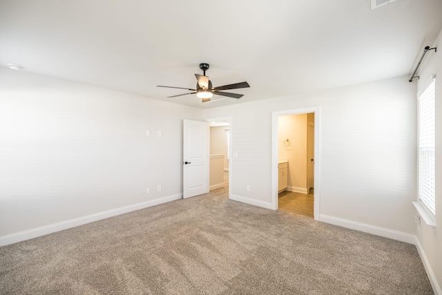 unfurnished bedroom with light carpet, connected bathroom, a walk in closet, and ceiling fan