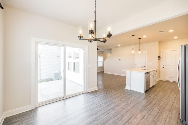 kitchen with sink, appliances with stainless steel finishes, a kitchen island with sink, light hardwood / wood-style floors, and decorative light fixtures