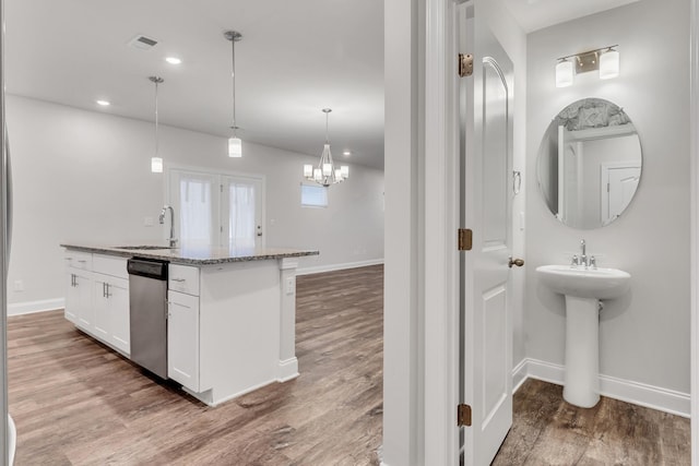 kitchen with hardwood / wood-style flooring, white cabinetry, a kitchen island with sink, decorative light fixtures, and stainless steel dishwasher