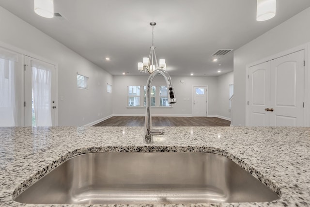 kitchen featuring sink, hanging light fixtures, a notable chandelier, hardwood / wood-style flooring, and light stone countertops