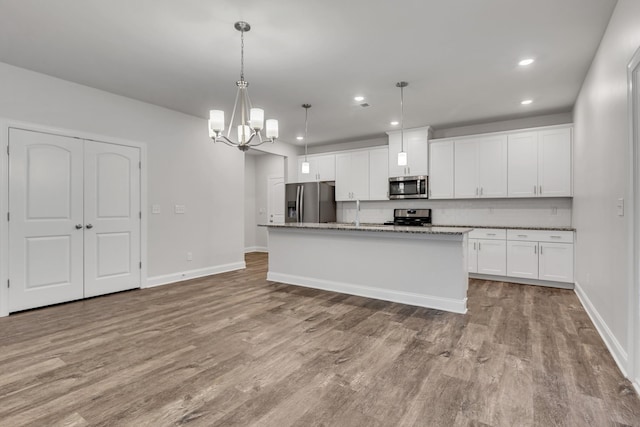 kitchen featuring hanging light fixtures, a center island with sink, stainless steel appliances, light stone countertops, and white cabinets