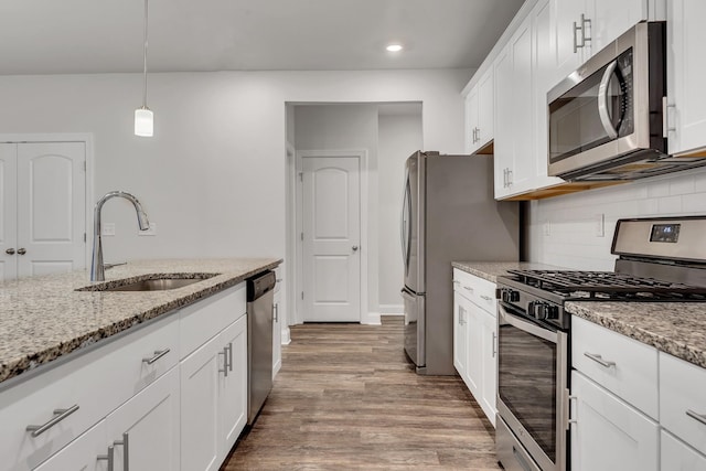 kitchen with pendant lighting, sink, white cabinets, stainless steel appliances, and light stone countertops