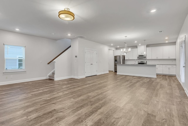 unfurnished living room featuring an inviting chandelier and light wood-type flooring