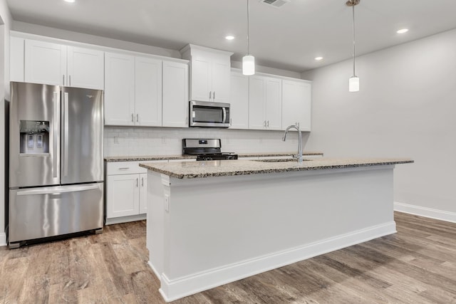 kitchen with a kitchen island with sink, hanging light fixtures, stainless steel appliances, and white cabinets