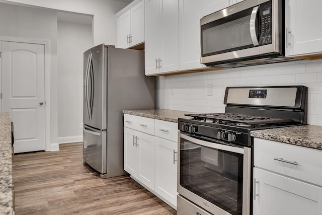 kitchen featuring appliances with stainless steel finishes, tasteful backsplash, white cabinetry, light stone counters, and light hardwood / wood-style floors