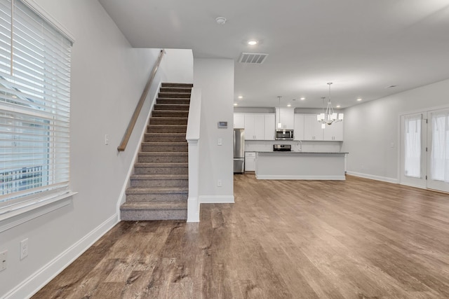 unfurnished living room featuring sink, light hardwood / wood-style flooring, and a notable chandelier