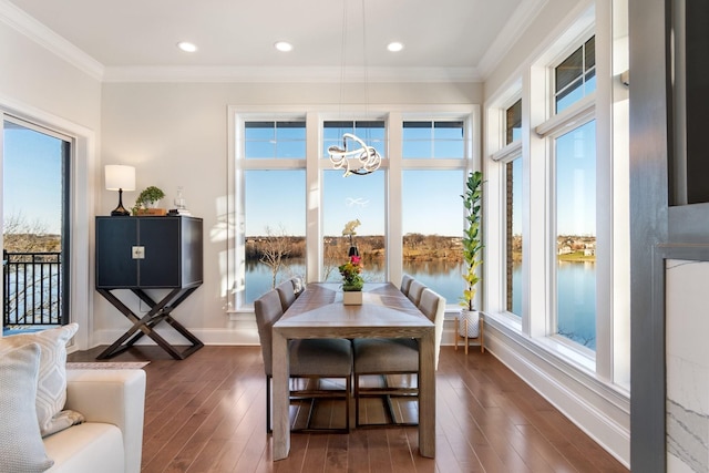 dining space with a water view, a healthy amount of sunlight, crown molding, and dark wood-type flooring