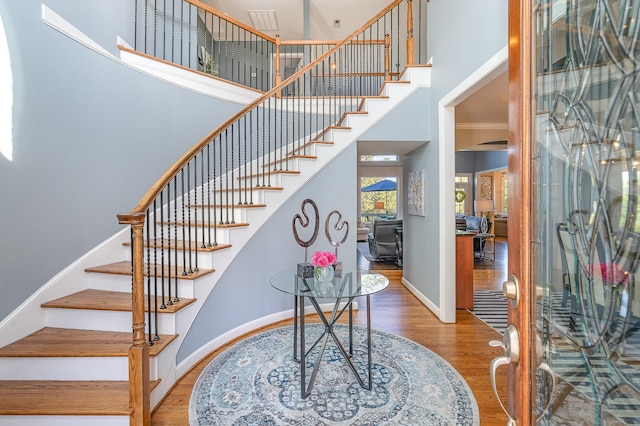 stairs featuring baseboards, wood finished floors, a towering ceiling, and crown molding