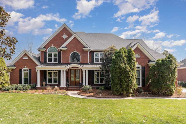 view of front facade featuring a front yard, brick siding, and roof with shingles