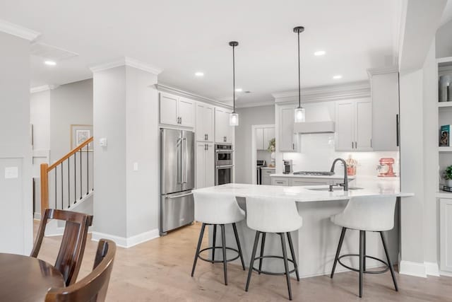 kitchen with decorative light fixtures, white cabinets, stainless steel appliances, a kitchen island with sink, and wall chimney range hood