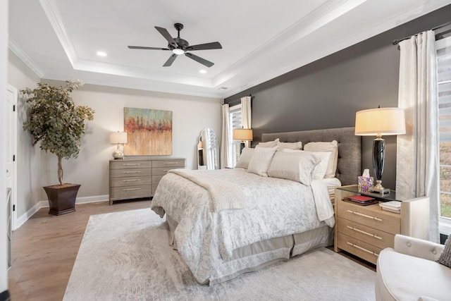 bedroom featuring multiple windows, ornamental molding, light hardwood / wood-style floors, and a raised ceiling