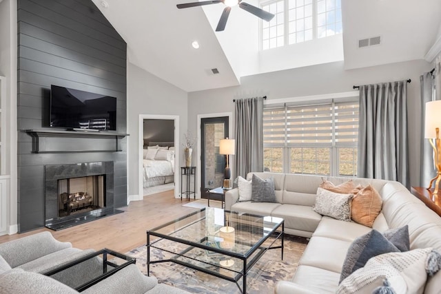 living room featuring high vaulted ceiling, a large fireplace, ceiling fan, and light hardwood / wood-style flooring