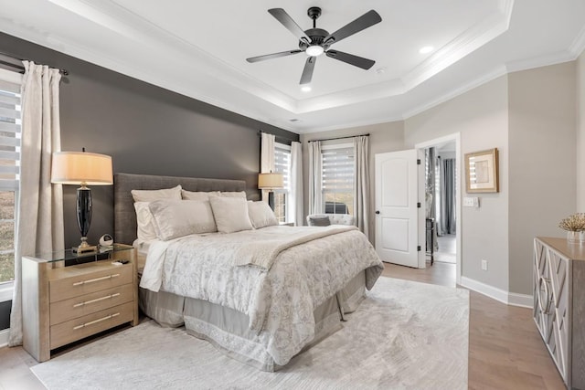 bedroom featuring light hardwood / wood-style flooring, ornamental molding, a raised ceiling, and ceiling fan