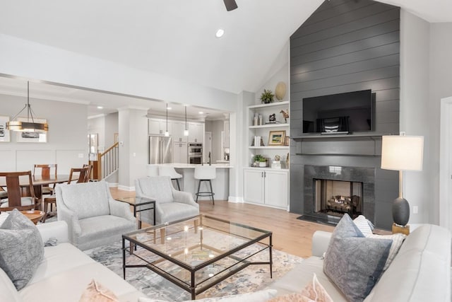 living room with lofted ceiling, crown molding, light wood-type flooring, a notable chandelier, and a fireplace