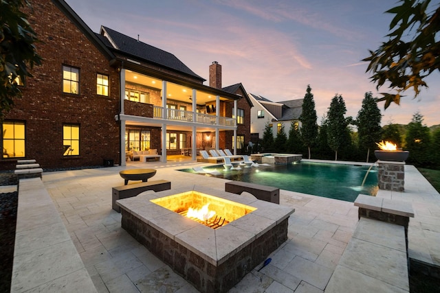 pool at dusk with pool water feature, an in ground hot tub, a patio area, and a fire pit