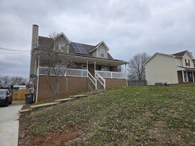 view of front of house with cooling unit, a porch, a front yard, and solar panels