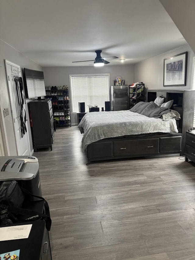 bedroom with wood-type flooring, stainless steel fridge, and ceiling fan