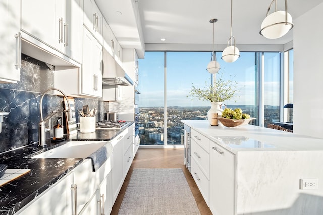 kitchen featuring dark wood-type flooring, white cabinetry, backsplash, decorative light fixtures, and stainless steel gas stovetop