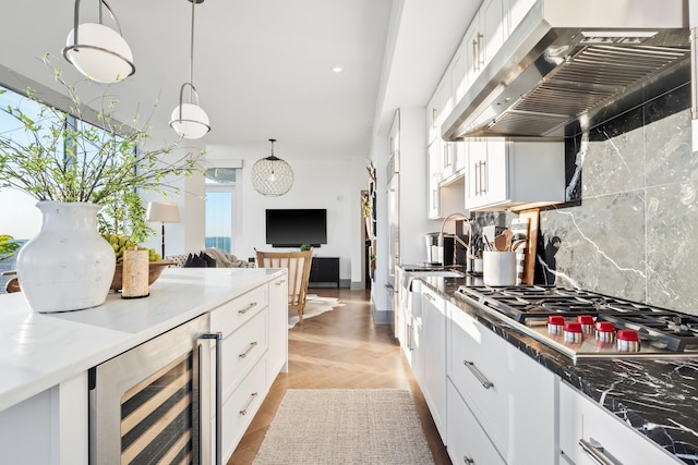 kitchen with stainless steel gas stovetop, white cabinetry, beverage cooler, and range hood