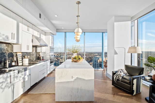 kitchen featuring sink, a kitchen island, white cabinets, pendant lighting, and backsplash