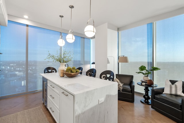 kitchen with pendant lighting, white cabinets, expansive windows, a center island, and light stone counters