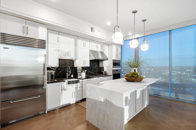 kitchen featuring appliances with stainless steel finishes, hanging light fixtures, tasteful backsplash, white cabinets, and a kitchen island