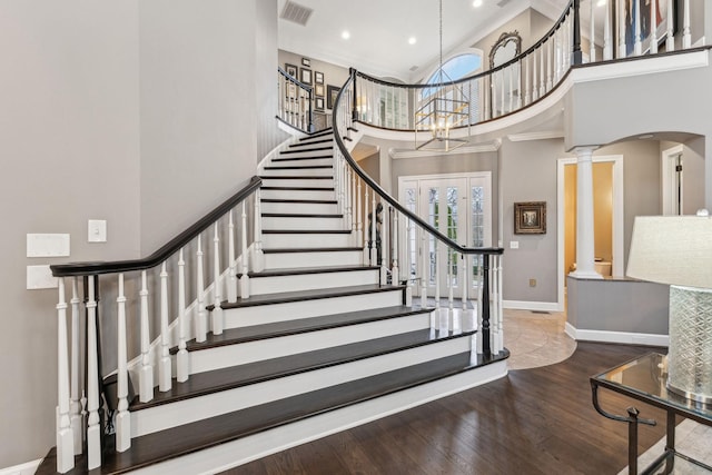 stairs with hardwood / wood-style flooring, a notable chandelier, decorative columns, and a high ceiling