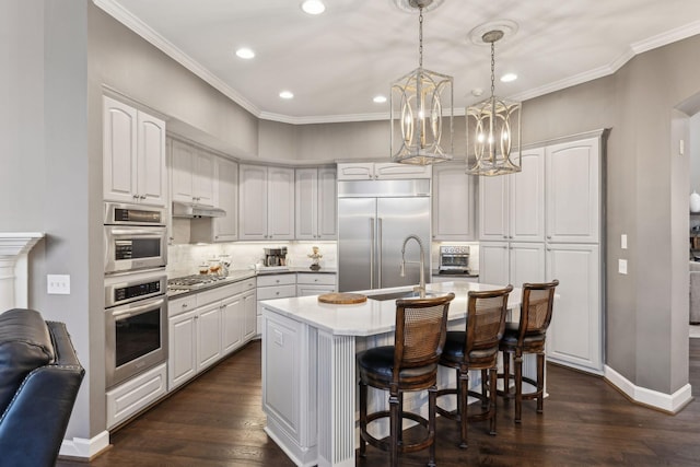 kitchen with a kitchen island with sink, white cabinetry, stainless steel appliances, and decorative light fixtures