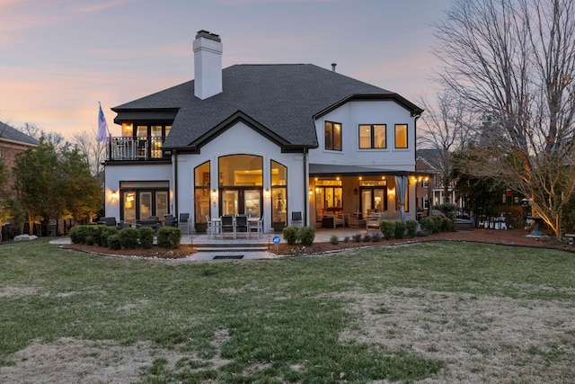 back house at dusk featuring a yard, a patio, and a balcony