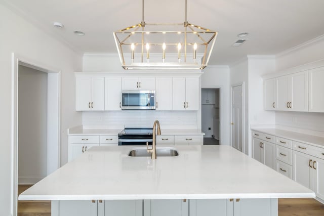 kitchen featuring appliances with stainless steel finishes, a center island with sink, white cabinets, and decorative light fixtures