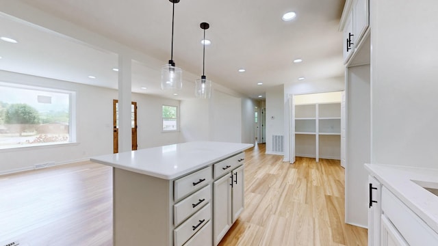 kitchen with a kitchen island, light wood-type flooring, hanging light fixtures, and white cabinets