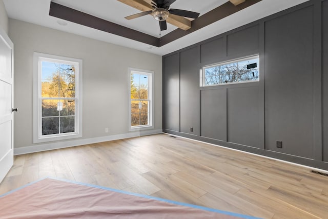 empty room with a ceiling fan, visible vents, baseboards, light wood-type flooring, and a raised ceiling