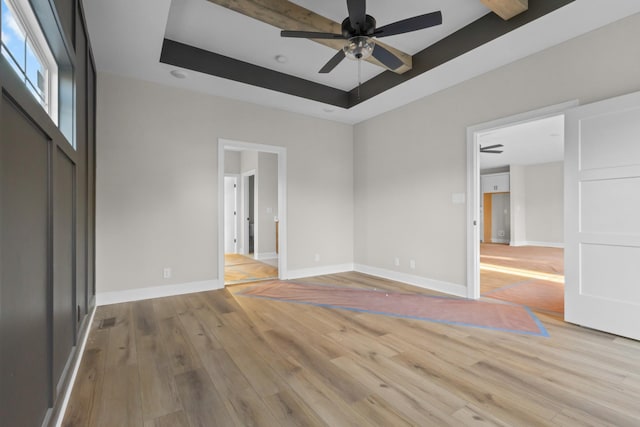 unfurnished bedroom with light wood finished floors, a tray ceiling, visible vents, and baseboards