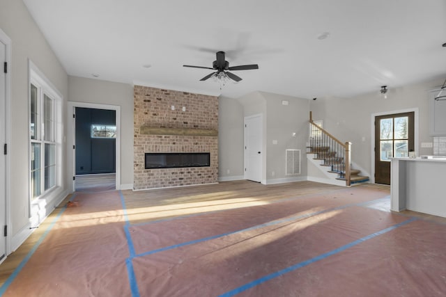 unfurnished living room with visible vents, a ceiling fan, a brick fireplace, baseboards, and stairs