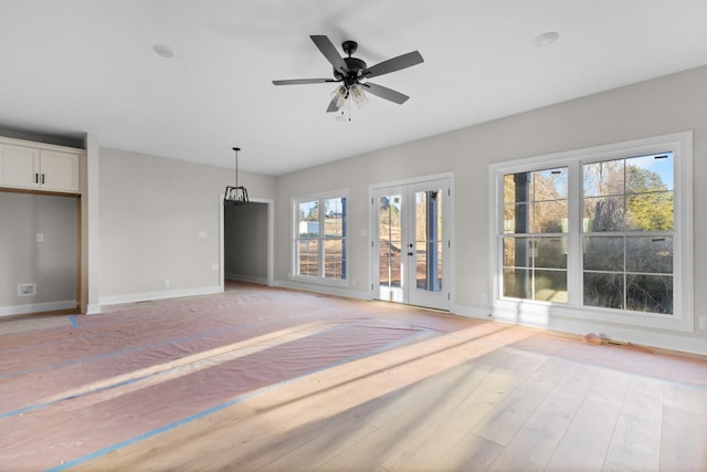 unfurnished living room with light wood-type flooring, ceiling fan, baseboards, and french doors