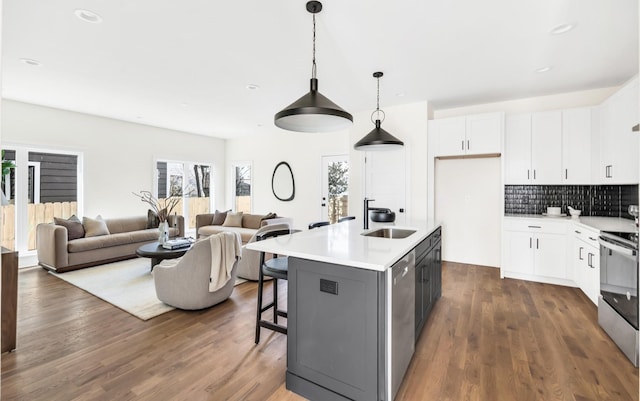 kitchen featuring sink, appliances with stainless steel finishes, an island with sink, white cabinets, and decorative light fixtures