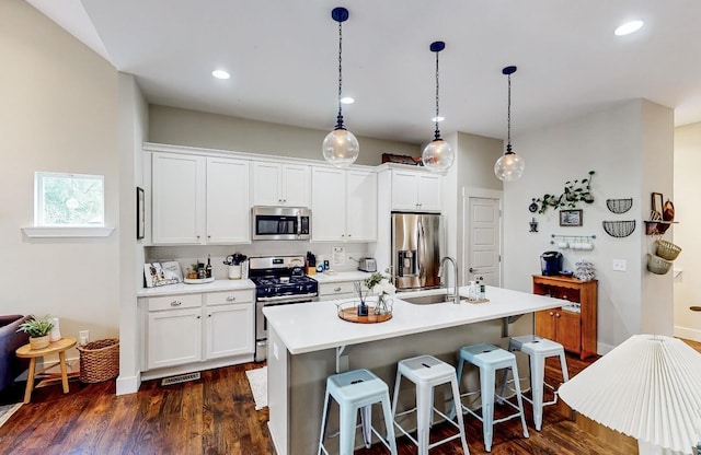 kitchen with stainless steel appliances, decorative light fixtures, a kitchen island with sink, and white cabinets