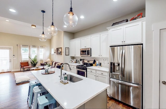 kitchen featuring sink, white cabinetry, decorative light fixtures, appliances with stainless steel finishes, and a kitchen island with sink