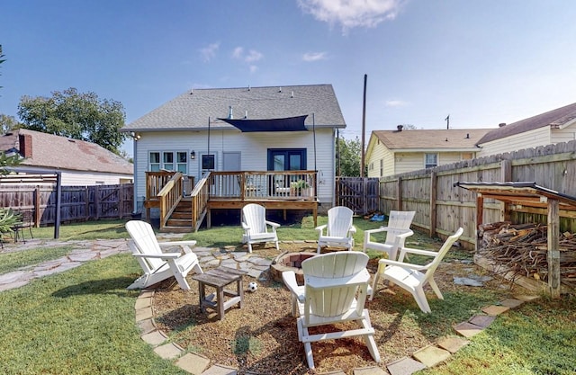 back of property with a wooden deck, an outdoor fire pit, and a lawn