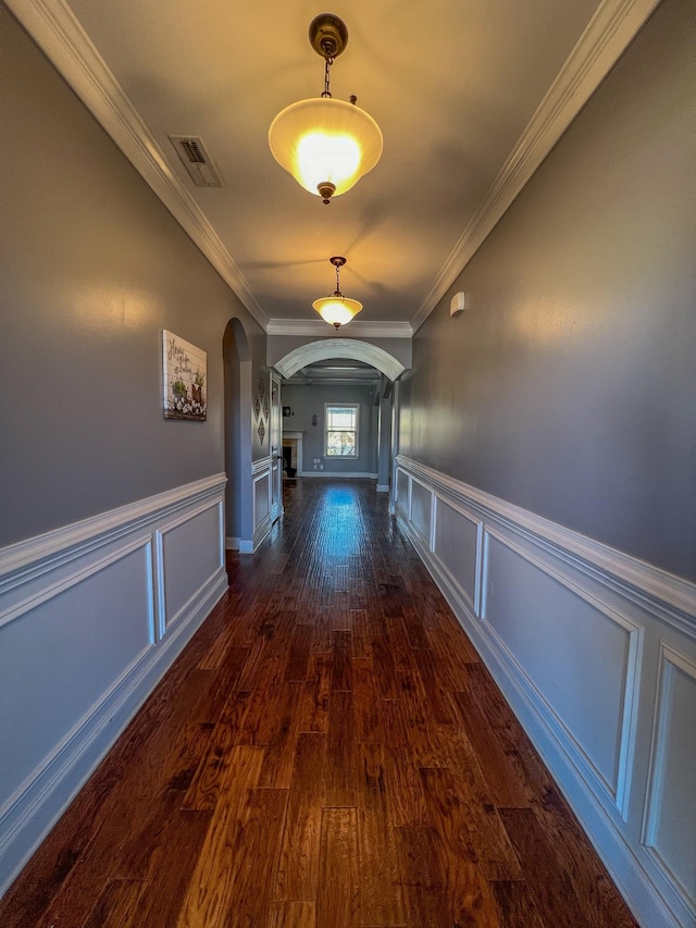 hallway featuring arched walkways, visible vents, crown molding, and dark wood-style flooring