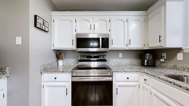 kitchen with light stone countertops, a textured ceiling, stainless steel appliances, and white cabinets