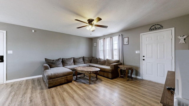 living room with a textured ceiling, ceiling fan, and light wood-type flooring