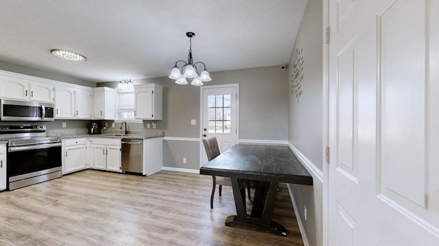 kitchen with pendant lighting, sink, white cabinetry, stainless steel appliances, and light wood-type flooring