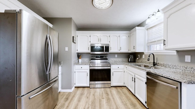 kitchen featuring sink, white cabinetry, appliances with stainless steel finishes, light stone countertops, and light hardwood / wood-style floors