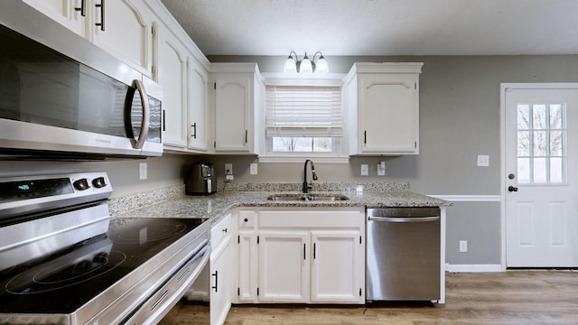 kitchen with sink, white cabinets, light stone counters, light hardwood / wood-style floors, and stainless steel appliances