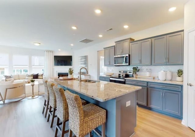 kitchen with sink, a breakfast bar area, appliances with stainless steel finishes, light hardwood / wood-style floors, and an island with sink