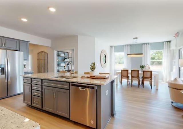 kitchen featuring gray cabinets, decorative light fixtures, sink, stainless steel appliances, and a center island with sink