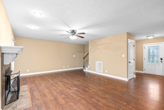 unfurnished living room with a tile fireplace, hardwood / wood-style floors, ceiling fan, and a textured ceiling