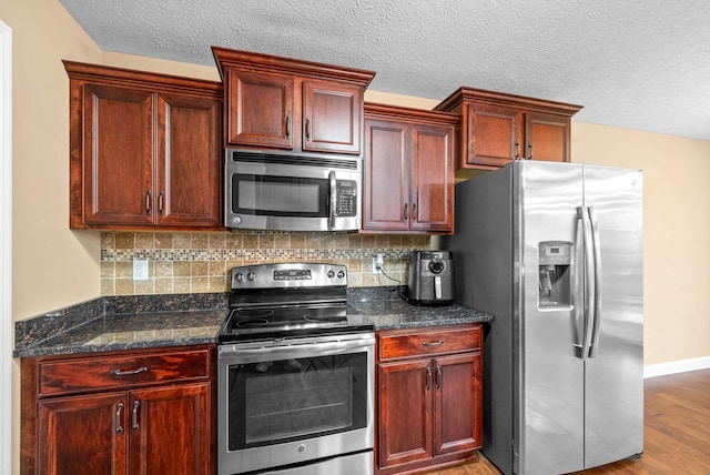 kitchen featuring tasteful backsplash, a textured ceiling, appliances with stainless steel finishes, dark stone counters, and light hardwood / wood-style floors