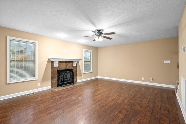 unfurnished living room with ceiling fan, a fireplace, dark hardwood / wood-style flooring, and a textured ceiling